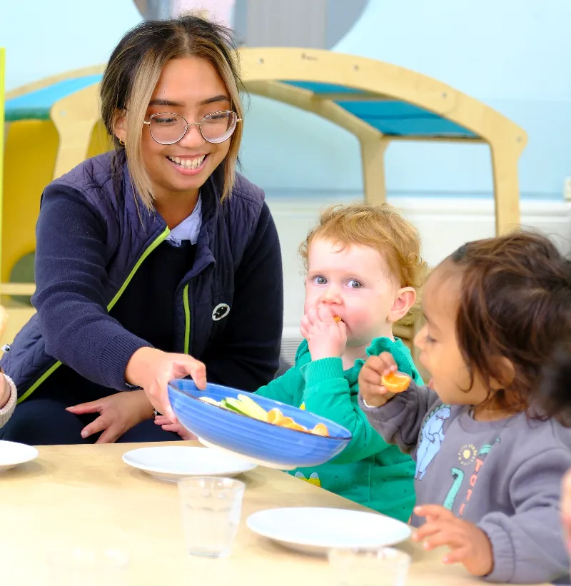 person holding out plate of fruit to two children